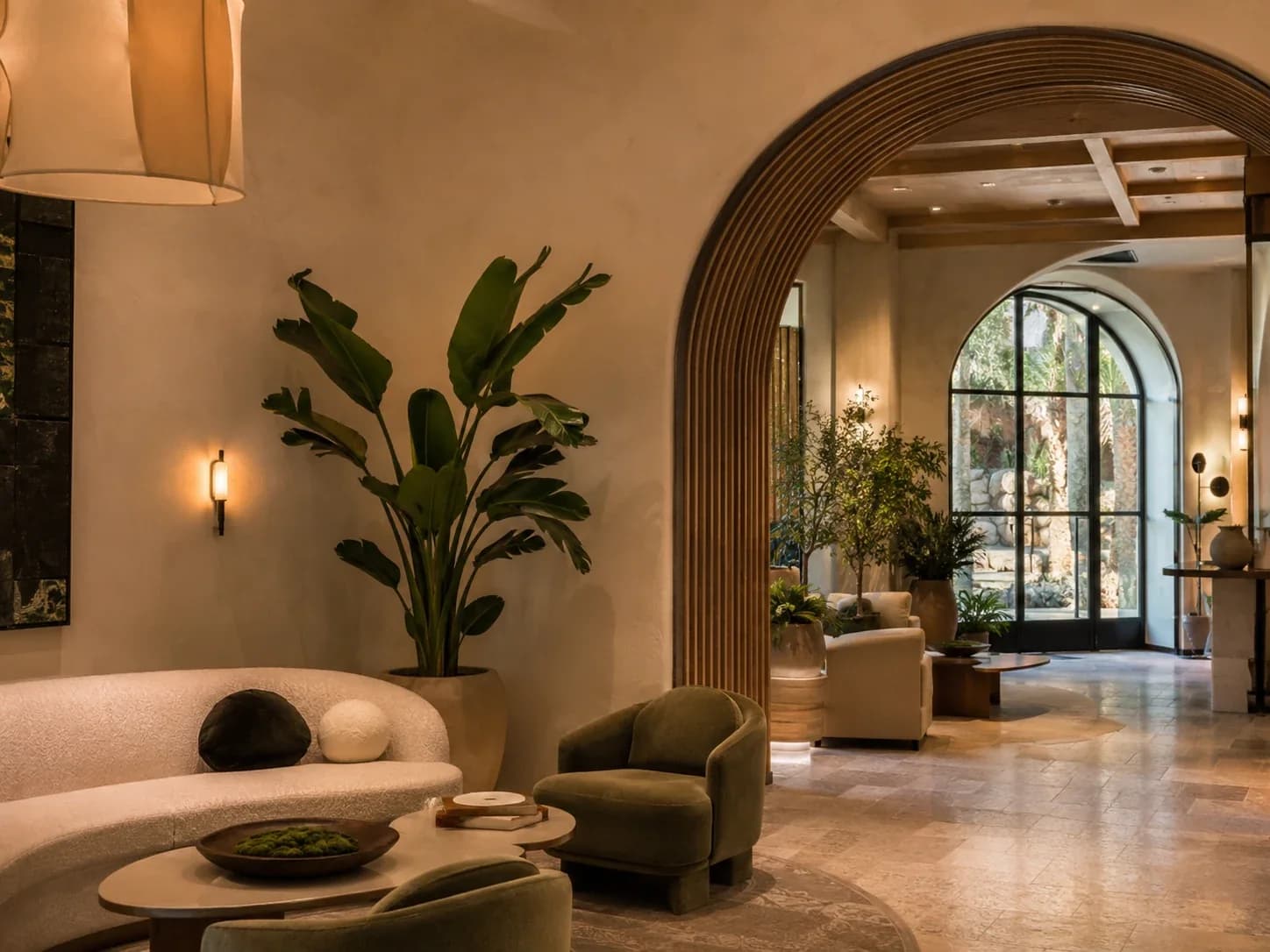 Hotel lounge with a fluted timber arch, curved boucle seating, olive velvet chairs and a planted courtyard beyond.